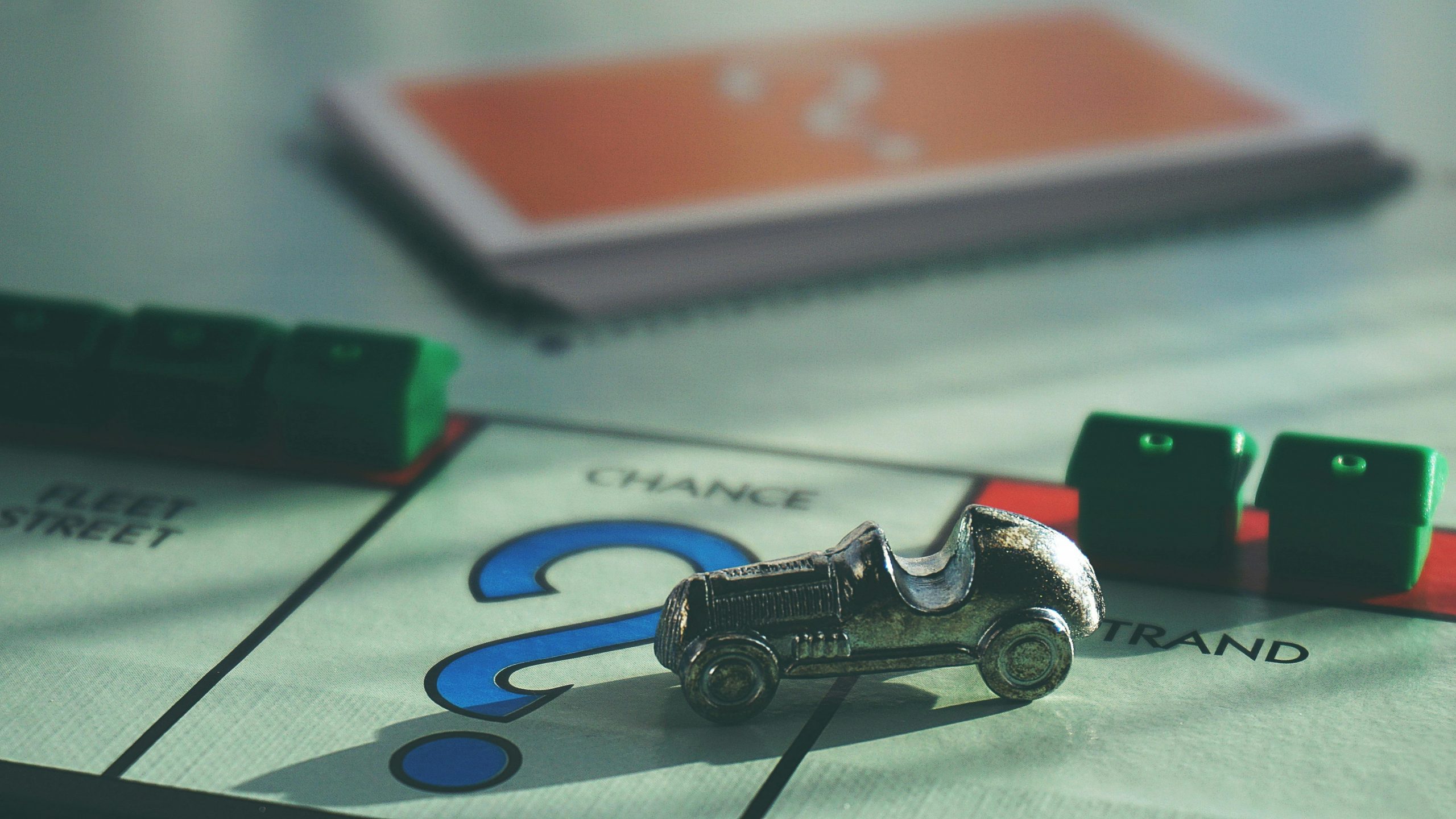 a car token, green house pieces, and cards on a Monopoly board