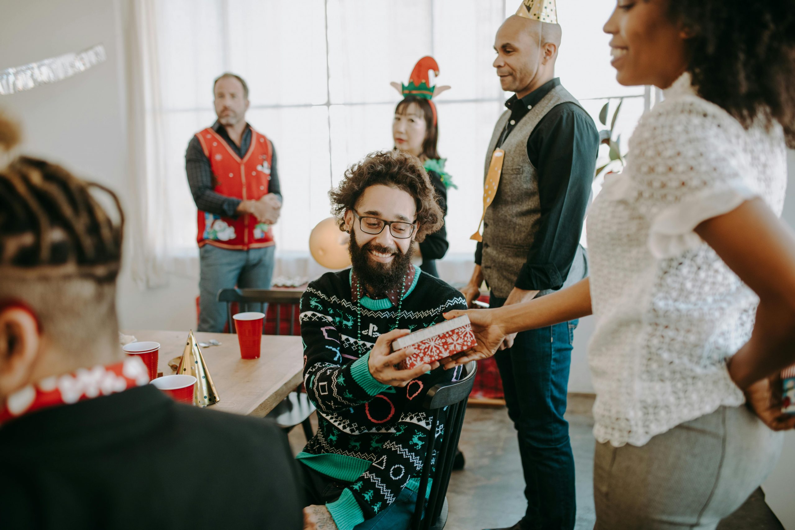 man handing a gift to a woman from behind, with family members in Christmas costumes nearby