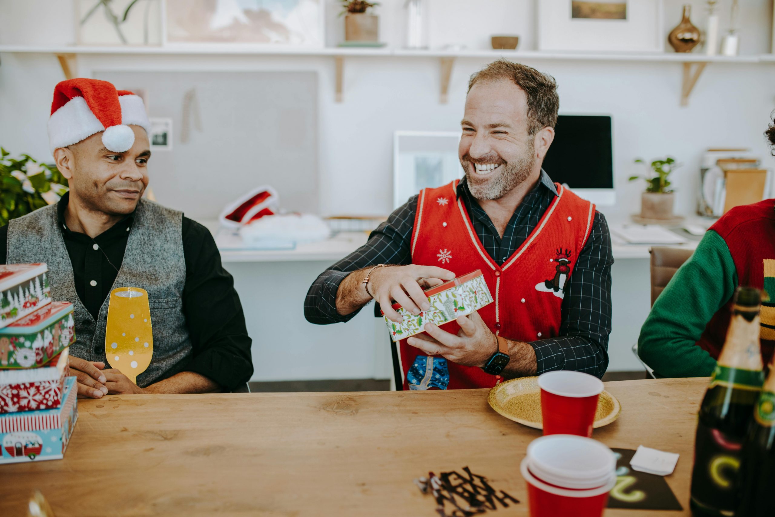 man smiling brightly while holding a wrapped present at a table, surrounded by his family